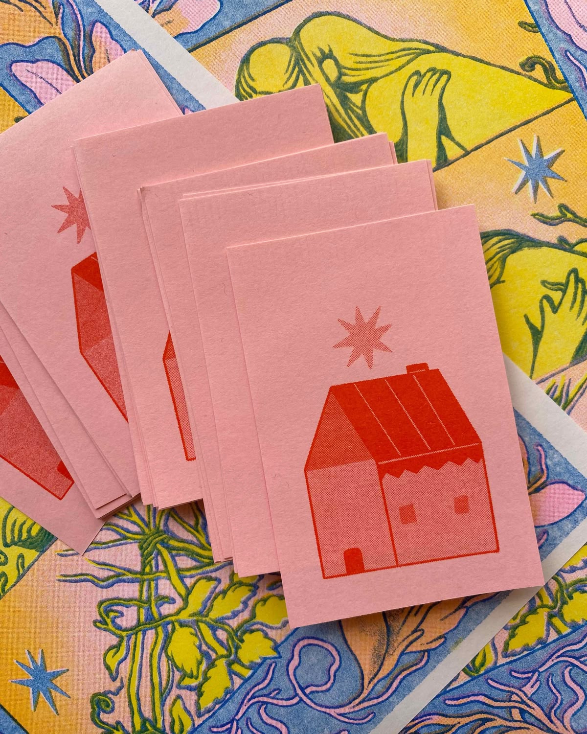A stack of pink risograph cards printed with a little red house